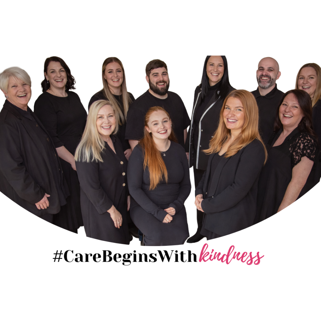 Group of eleven adults dressed in black, standing and smiling at the camera. Text below reads: #CareBeginsWithKindness.