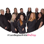 Group of eleven adults dressed in black, standing and smiling at the camera. Text below reads: #CareBeginsWithKindness.