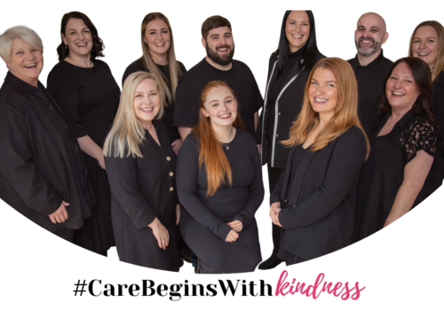 Group of eleven adults dressed in black, standing and smiling at the camera. Text below reads: #CareBeginsWithKindness.