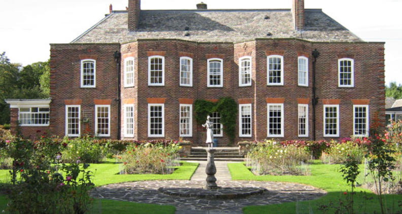 A large brick Georgian-style house with many white-framed windows, a central fountain, and landscaped gardens in the foreground.