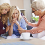 Three women sitting on a couch talking to each other.