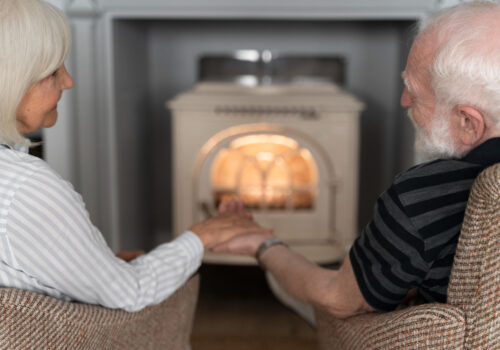 elderly couple hold hands in front of fire