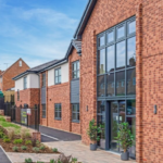 Newly constructed modern brick block of flats with large windows, a paved entrance, and landscaped garden beds near a residential road.