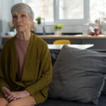 sad looking older lady sits alone on sofa