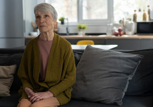 sad looking older lady sits alone on sofa