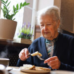 Portrait of a 90-year-old grey haired senior lady dining in a restaurant. Soup, main course, tea. Conversation.
